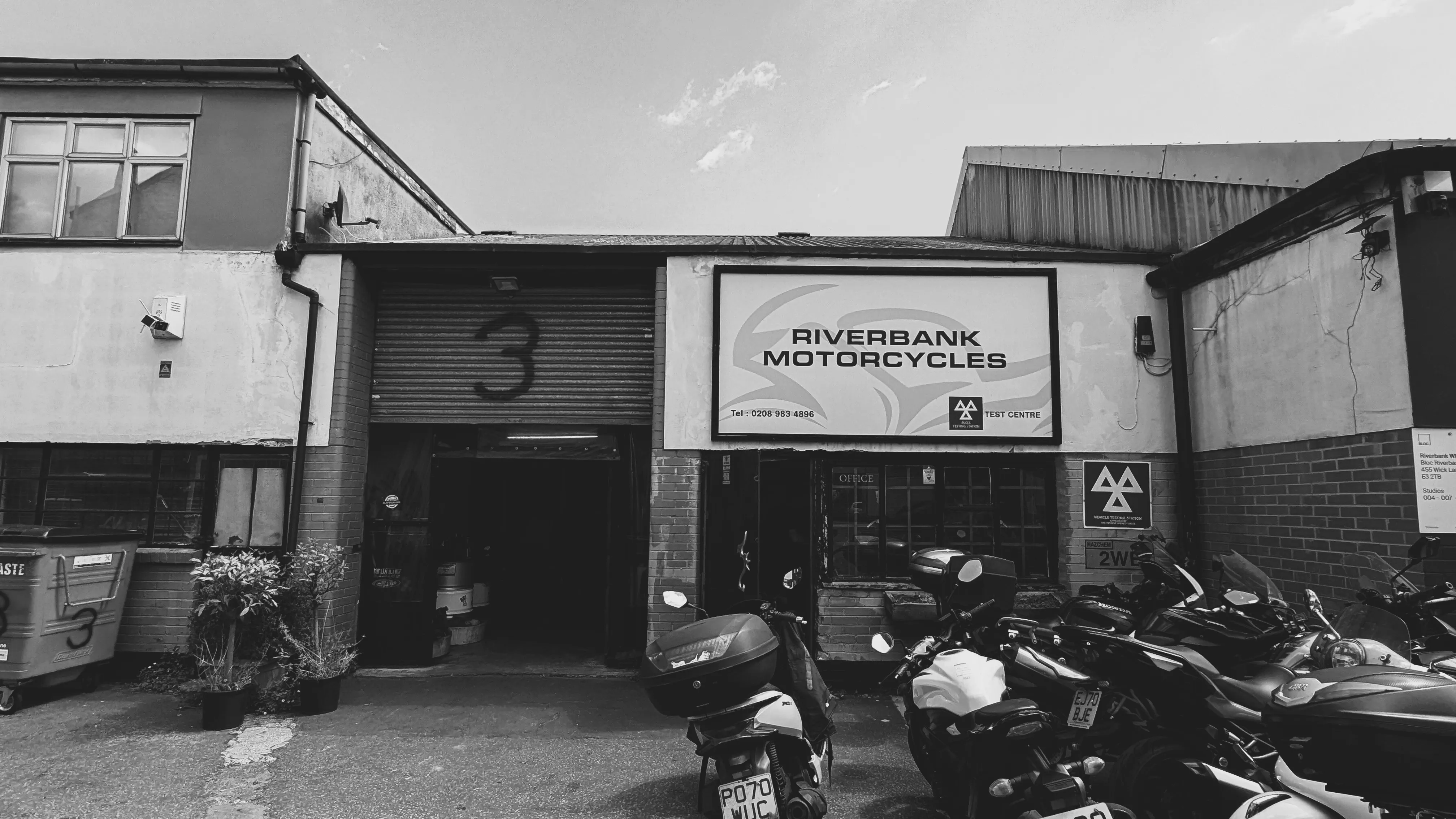The Riverbank Motorcycles workshop entrance and signage in Bow, East London, with motorcycles parked outside